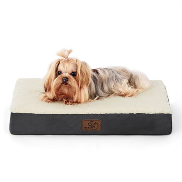 Small fluffy dog with pink bow relaxing on a large gray and cream orthopedic dog bed.
