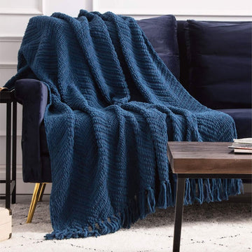 GentleSoft blue chenille knit throw blanket with chevron texture and tassels on sofa.