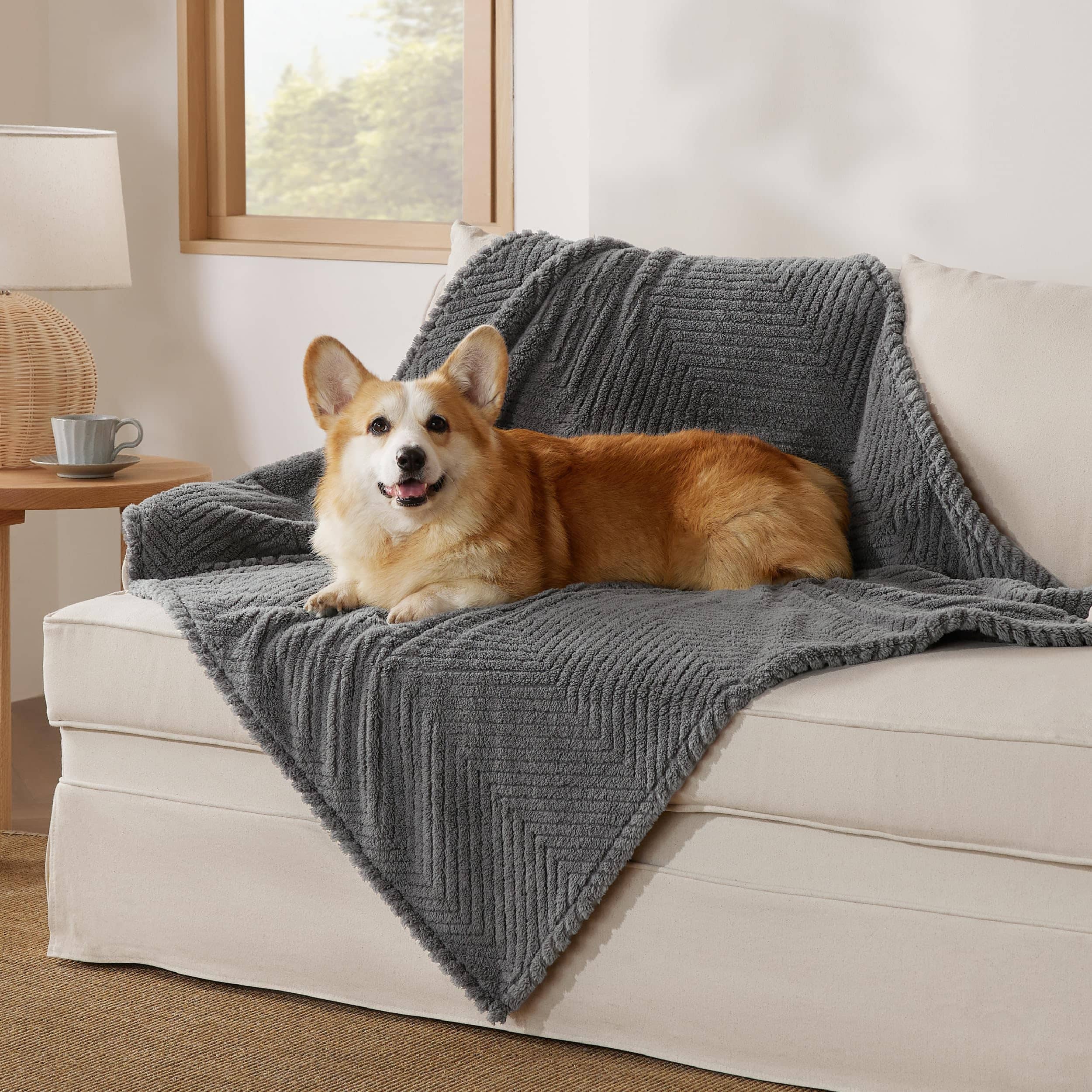 Dark grey jacquard fleece pet blanket with chevron pattern protecting a cream sofa with a happy Corgi resting on it.
